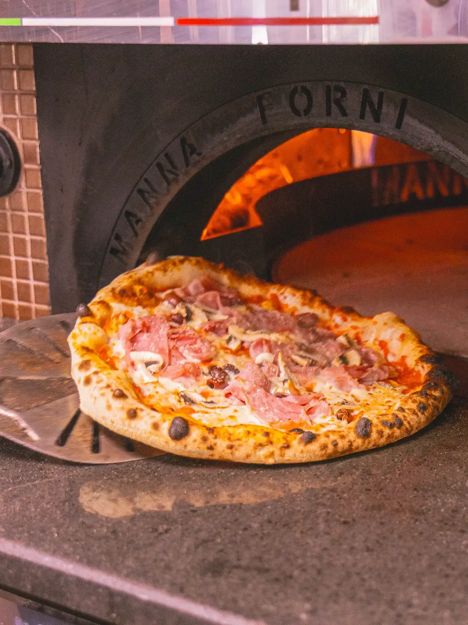 Une pizza entre dans le four à bois